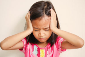 menina usando blusa cor de rosa coloca as mãos ao lado das cabeças representando uma dor de cabeça um dos sintomas da meningite